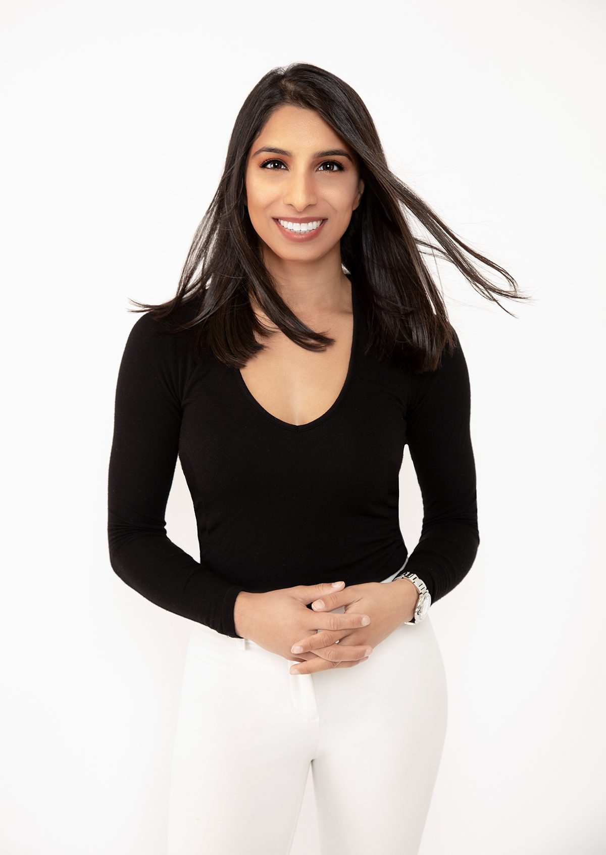Modern personal branding portrait of a woman wearing business casual dress with white pants on a white background. The subjects hair is blowing and she is smiling and approachable. Personal Branding Photography by Andrea Liora Studios in San Francisco.