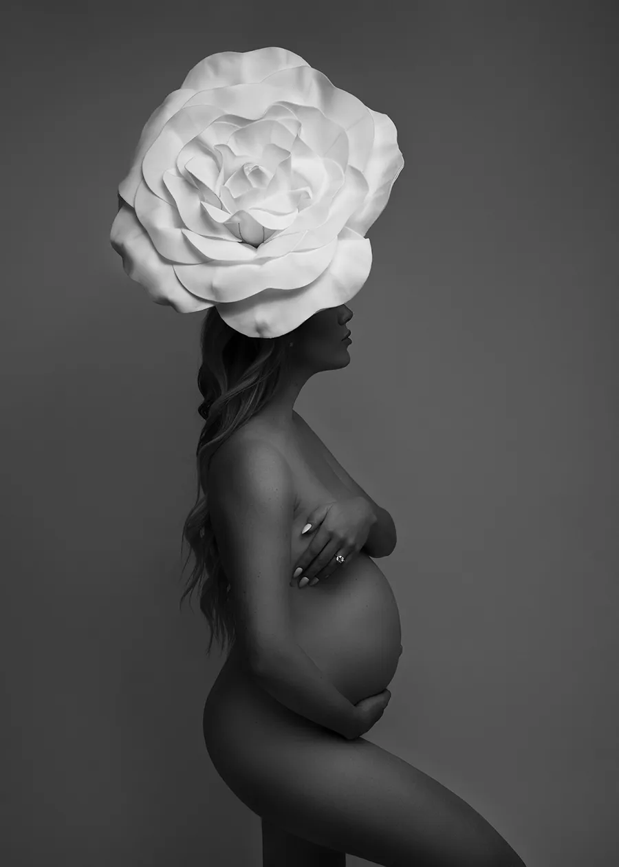Black and white nude maternity portrait of a pregnant woman wearing a large white flower headpiece taken by Andrea Liora Studios in San Francisco CA.