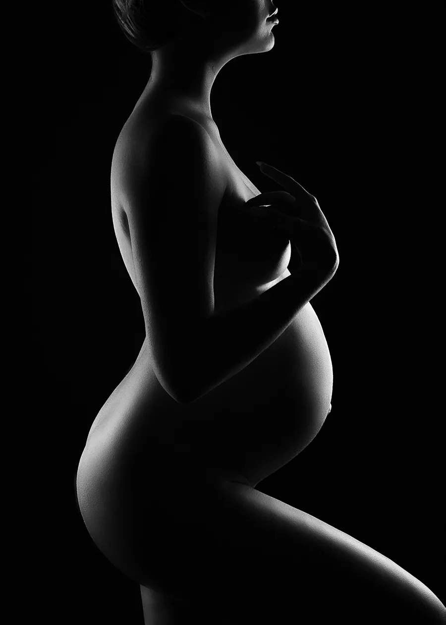Fine Art Nude black and white silhouette boudoir image of a pregnant woman with light shining on the front of her body.