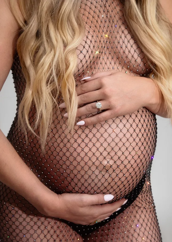 Boudoir photography close up of a pregnant womans belly showing her wedding ring and sparkling fishnet dress.