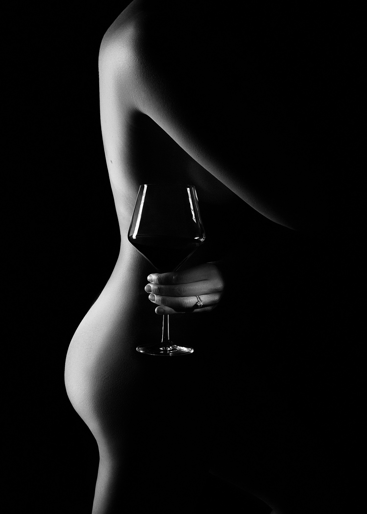 black and white boudoir silhouette of a nude woman with a wine glass and engagement ring lit dramatically.