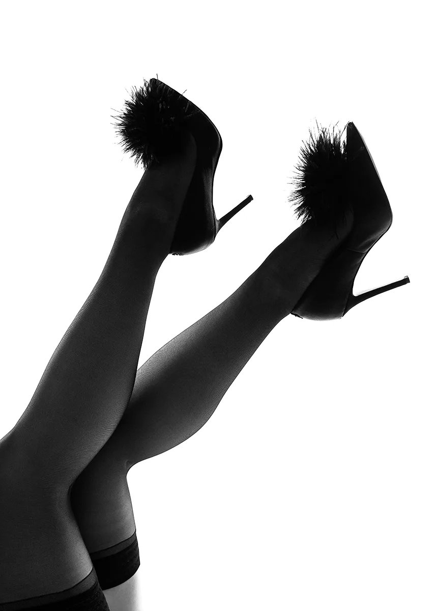 black and white artistic backlit boudoir photograph of a woman's upside down legs wearing thigh high stockings and high heel shoes.