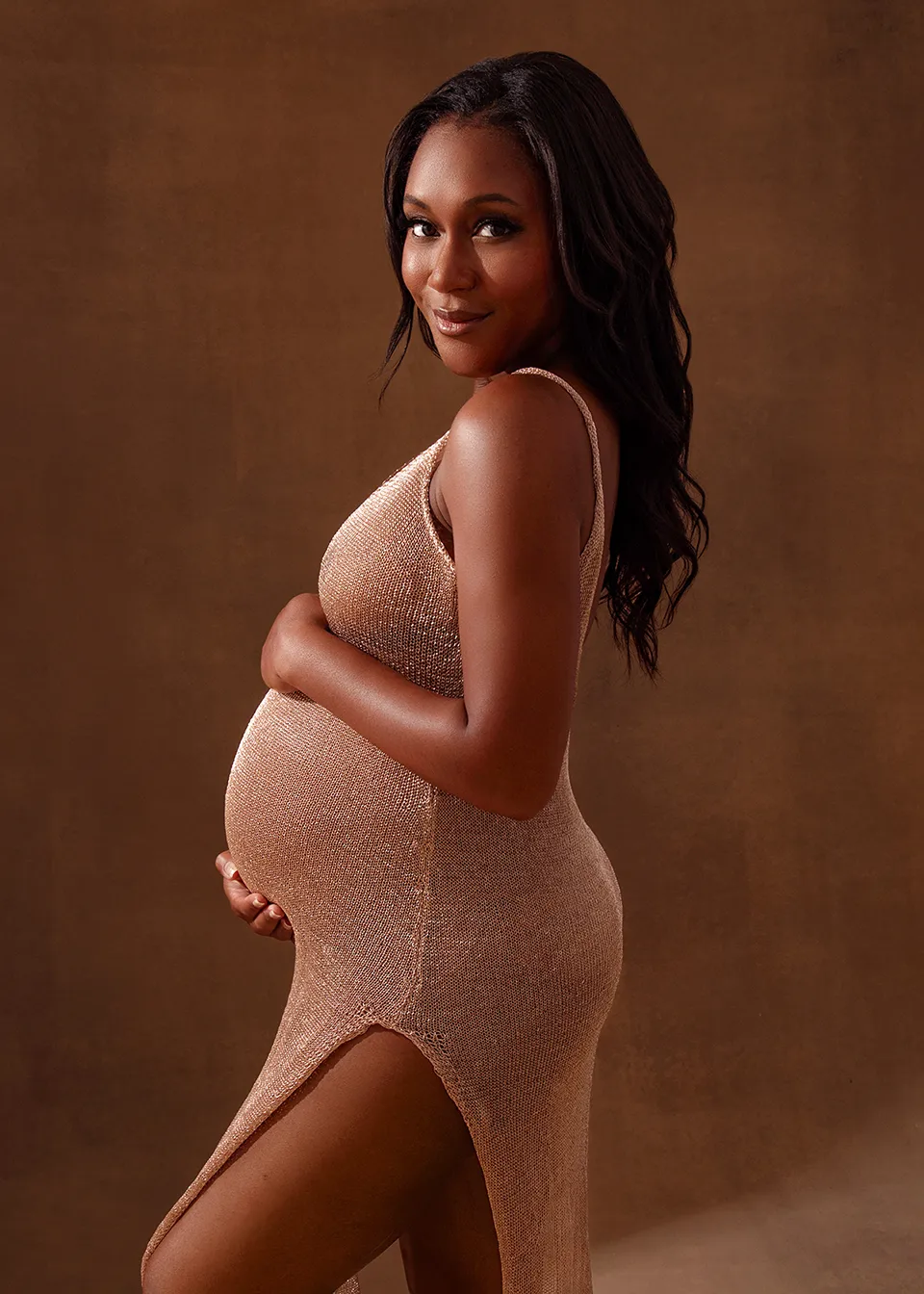 Maternity photograph of a pregnant woman wearing a golden dress with a golden background behind her. The portrait is a fashion inspired maternity photograph.